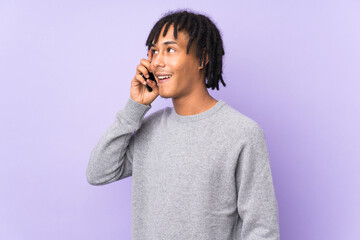 Wall Mural - Young african american man isolated on purple background keeping a conversation with the mobile phone