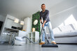 Young happy man vacuuming at home. Man cleaning house with vacuum cleaner. House keeping 