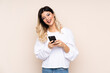 © luismolinero - Teenager girl isolated on beige background sending a message with the mobile