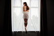 © andrey - Beautiful sexy girl in a white robe with long hair stands in the window opening