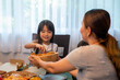 Happy Asian family relationship at home. Mother with little daughter and son eating fried chicken and pizza on the table. Parents with two child kids enjoy and having fun with lunch together at home.