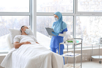 Wall Mural - Female Muslim doctor visiting male patient in clinic