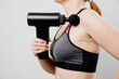 © Maria - woman holds massage gun. medical-sports device helps to reduce muscle pain after training, helps to relieve fatigue, affects problem areas of body, improves condition of skin.