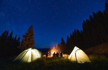 Wall Mural - rear view, tourists are sitting by brightly blazing bonfire between the tents against the backdrop o