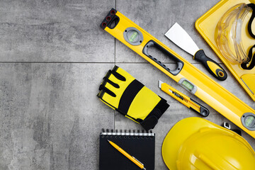 Contractor concept. Tool kit of the contractor: yellow hardhat, libella, hand saw on the gray tiles background.