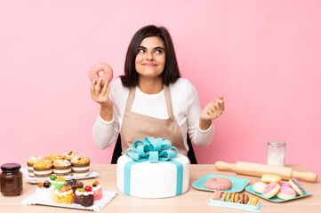 Pastry chef with a big cake in a table over isolated pink background