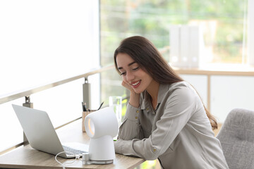 Canvas Print - Young woman enjoying air flow from portable fan at workplace. Summer heat