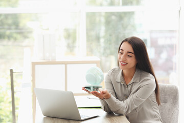 Wall Mural - Young woman enjoying air flow from portable fan at workplace, space for text. Summer heat