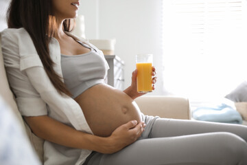 Wall Mural - Young pregnant woman with glass of juice in living room, closeup. Taking care of baby health