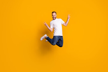 Wall Mural - Full length body size photo of jumping cheerful male model showing peace sign with two fingers isolated vivid yellow color background