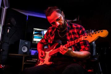 Canvas Print - Young man with beard is playing guitar in the stereo studio on the radio to record his new song