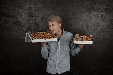 A guy in a white T-shirt holds boxes of pizza in his hands and greedily sniffs the smell on a black background. Young man eating a slice of pizza with closed eyes, isolated on yellow background.