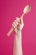 Female hand holds up a big wooden spoon on a pink background. Raised up clenched fist for protest. Put the power back in your hands, support concept.	