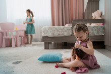 Cute Little Girl Playing With A Doll Whille Sitting On The Carpet In Her Room