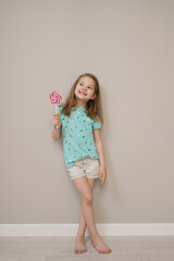 Happy young caucasian little girl kid with happy big sweet lollypop candy on beige background