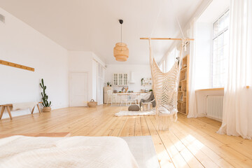 cute cozy light interior design of the apartment with a free layout of the kitchen and bedroom areas. a lot of windows, a wooden floor and a hanging swing.