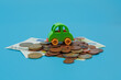 Green mini toy car on coins and banknotes on blue background. Buying car concept