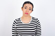 © Roquillo - Displeased upset Young beautiful woman wearing stripped t-shirt against white wall frowns face as going to cry, being discontent and unhappy as can't achieve goals,  Disappointed model has troubles