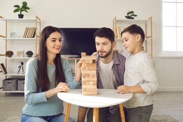 Happy young family with child enjoying quiet indoor activities on weekend at home. Smiling Caucasian couple with little son playing board game and having fun together