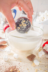 Hot chocolate bomb, with marshmallow and chocolates and nuts,  Woman's hand dropping chocolate bomb into cup with milk.