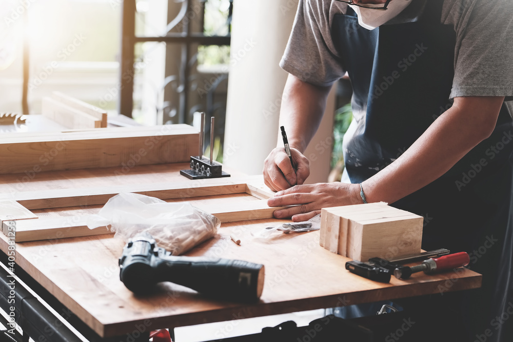 A carpenter measures the planks to assemble the parts, and build a wooden table for the customer - obrazy, fototapety, plakaty 
