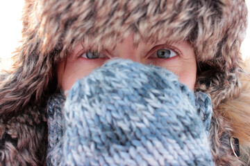 Portrait of a young woman in a fur cap with covered face outdoor. Close-up of eyes.
