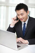 © eastfenceimage - Portrait of businessman sitting at desk and using cell phone