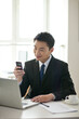 © eastfenceimage - Portrait of businessman sitting at desk and using cell phone