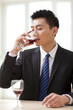 © eastfenceimage - Portrait of businessman at desk drinking a glass of wine