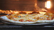 Male cook taking out four cheese pizza from electric oven using a shovel and putting it table at cuisine. Young cook baked delicious dish at kitchen restaurant. Concept of preparing food. Slow motion