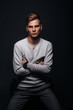 © qunica.com - Informally ( casual ) dressed blonde young man with sharp jawline in his 20's posing in a studio in front of a black background while wearing a white sweater.