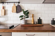 © KatrinaEra - Kitchen brass utensils, chef accessories. Hanging kitchen with white tiles wall and wood tabletop.Green plant on kitchen background