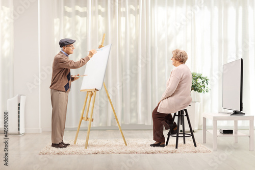 Elderly man painting a portrait of an elderly female model on a canvas