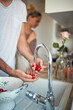 © luckybusiness - A young man washing fresh cherry tomatoes under the tap in the kitchen. Home, kitchen, salad