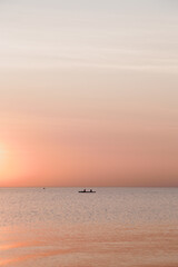 Sticker - Vertical shot of people in a boat in the calm sea during a scenic sunset