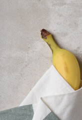 Ripe yellow banana wrapped in kitchen towel on gray mottled tile with copy space.