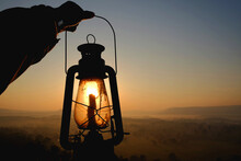 Silhouette Person Holding Lantern On Mountain Against Orange Sky