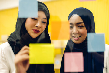 Wall Mural - Two muslim business woman planning and brainstorm writing over the project with stickers note on glass window at modern office.Teamwork concept