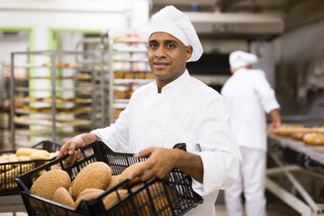 Wall Mural - Positive man baker carrying tray with fresh baked bread at bakery kitchen