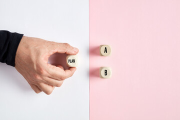 Wall Mural - Male hand holding a wooden cube with the word plan pointing at the options of A or B. Business plan decision or choice