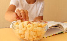 The Child's Hand Picks Up Corn Flakes Lying In A Glass Dish On The Background Of An Open Book