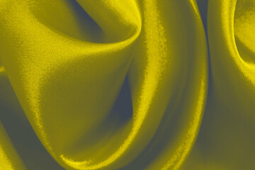 The abstract background is made of smooth elegant yellow silk satin. Close-up, random creases, selective focus.