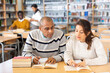 © JackF - Positive hispanic man and woman spending time together in library, talking, reading books and making notes