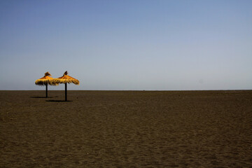 Panoramic view on empty deserted beach with two isolated thatch straw umbrellas - tourism industry prognosis outlook concept