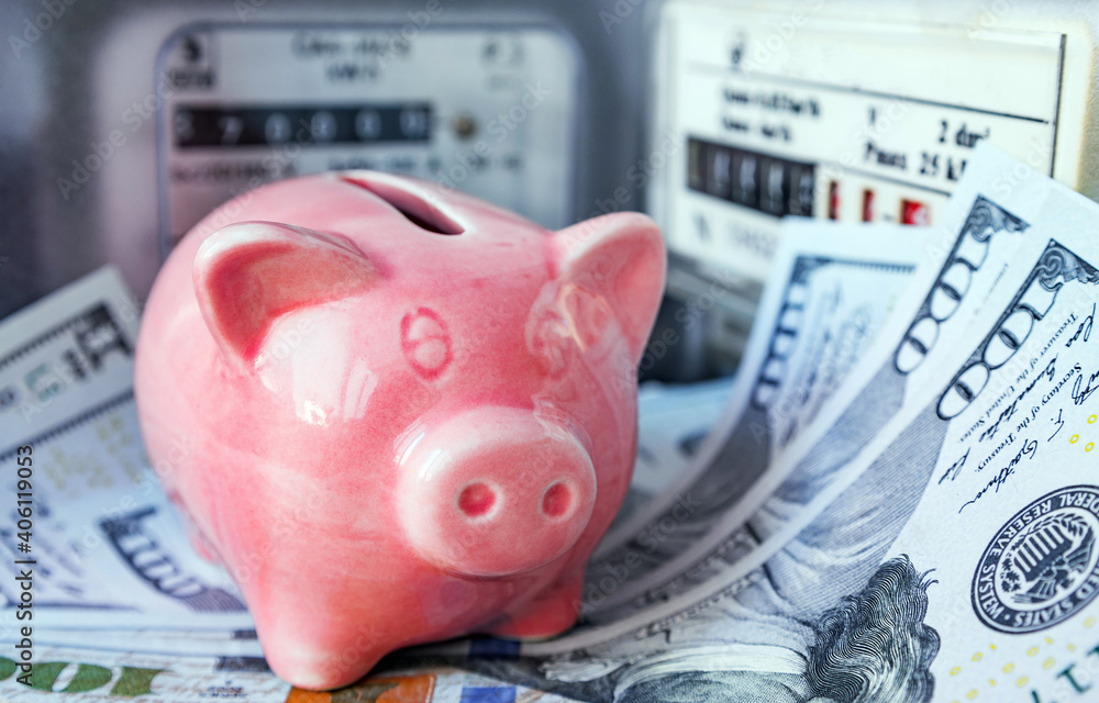 Pink piggy bank and US dollars near an electricity meter and gas meter ...