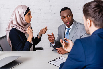 Sticker - multicultural businesspeople gesturing while discussing contract near interpreter, blurred foreground