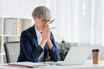 worried team leader in glasses with praying hands looking at laptop on desk