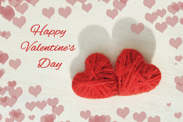 Two red hearts handmade from wool threads on a wooden light background