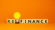 Refinance symbol. Wooden cubes with word 'refinance'. Yellow light bulb. Beautiful orange background. Business and refinance concept. Copy space.