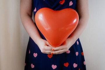 Young white woman holding heart shaped balloon against dress with hearts on it